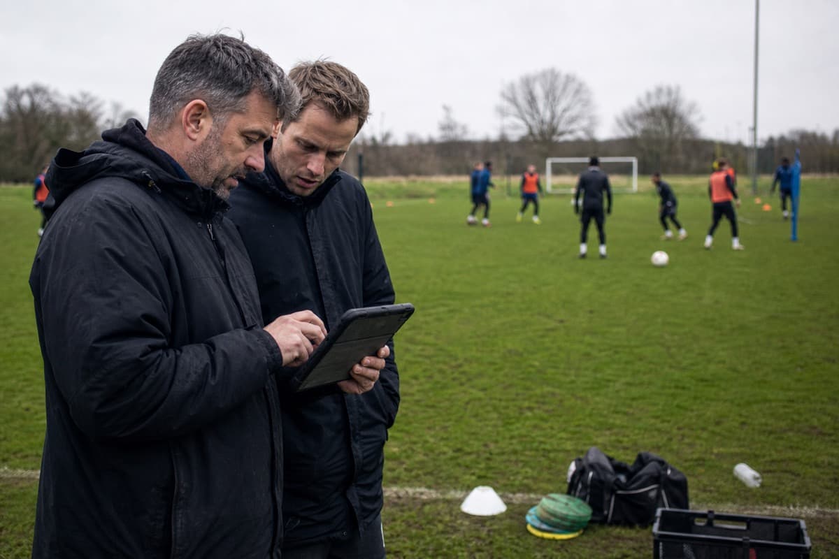 Football coaches reviewing training data beside a practice field