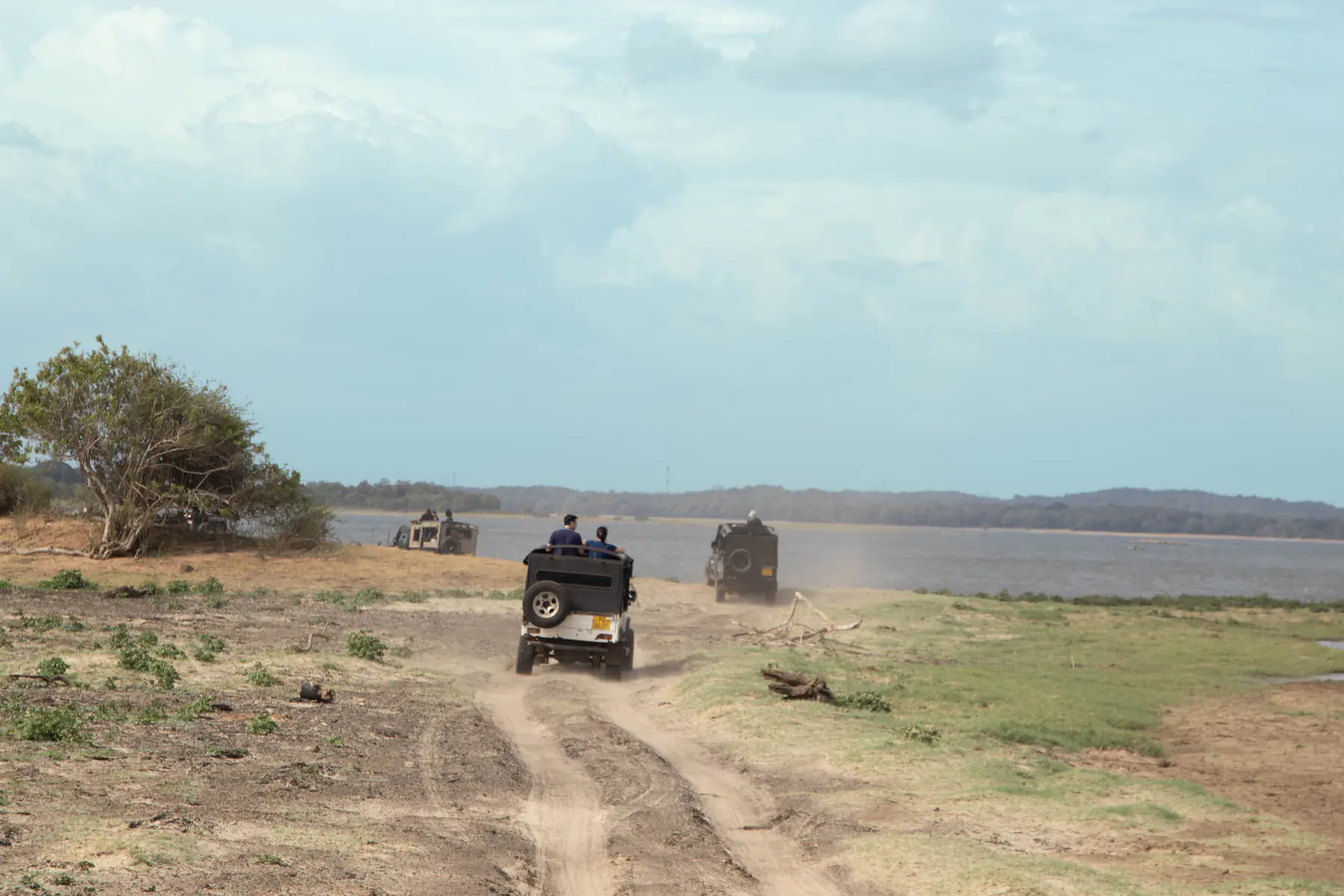 Two safari jeeps following a dusty trail beside the Minneriya reservoir