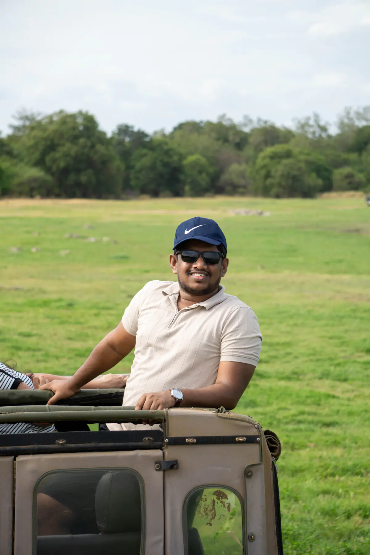 A man smiling from a safari jeep with an elephant behind him
