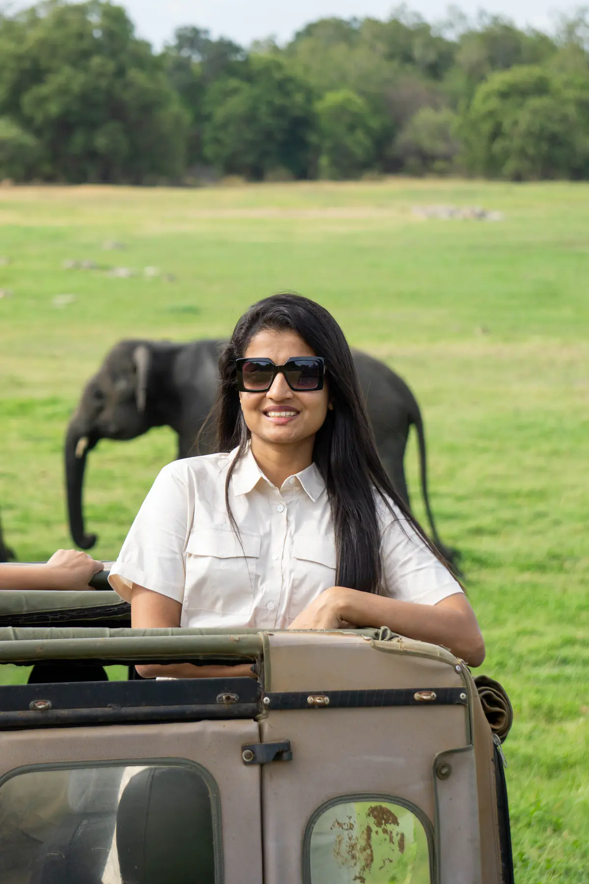 A woman smiling in a safari jeep with an elephant in the distance
